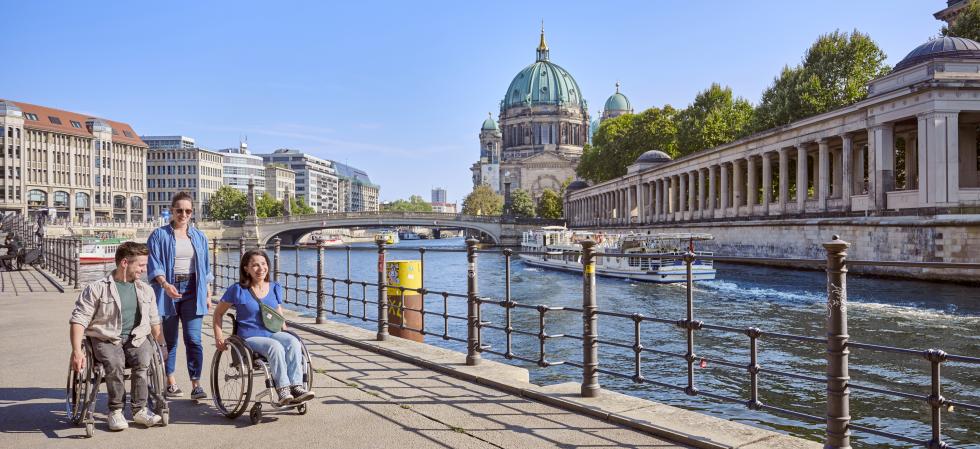 a group of friends, two on a wheelchair, strolling along the river Spree 